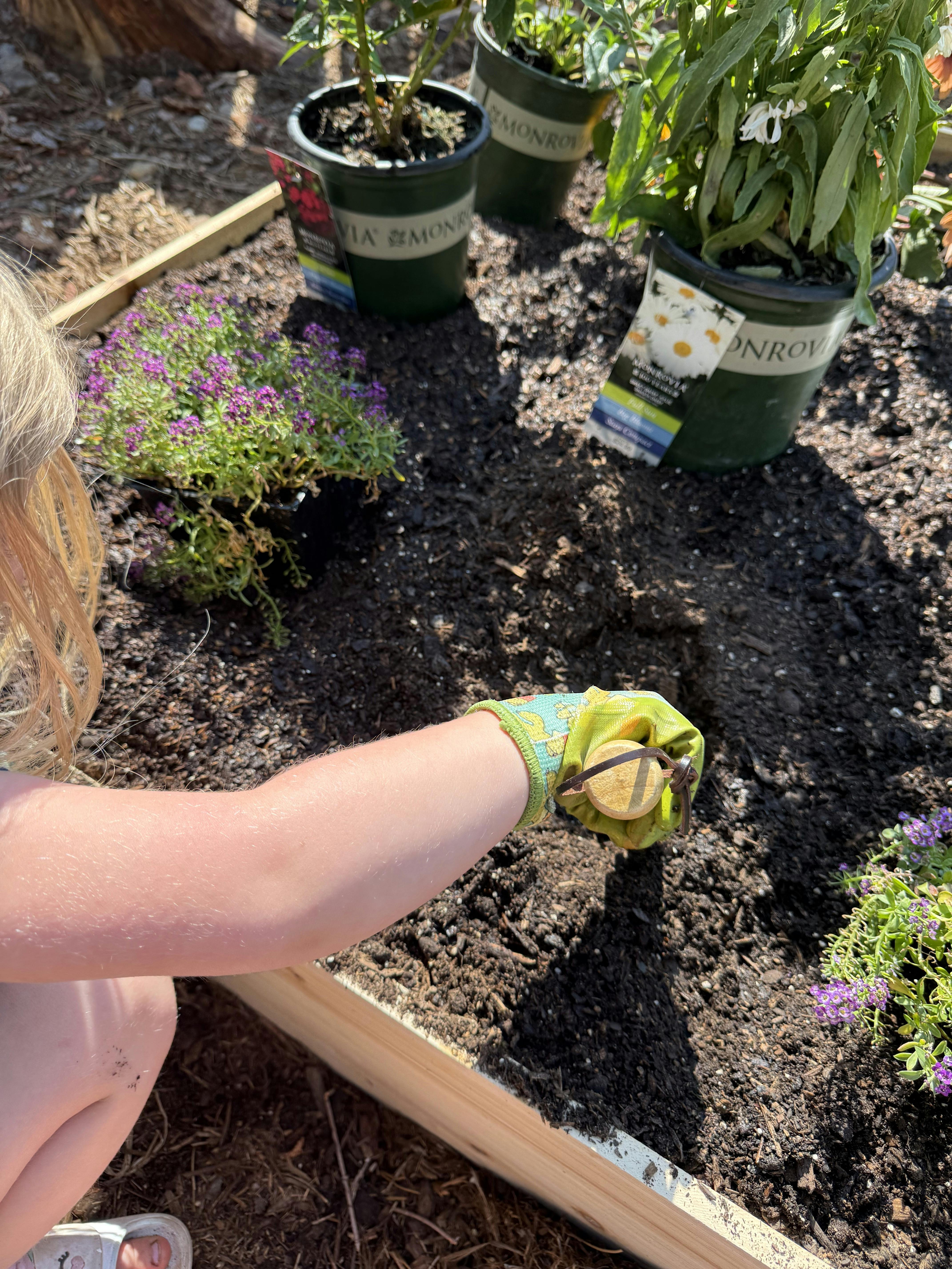 Child wearing gardening gloves digging in soil in a garden bed