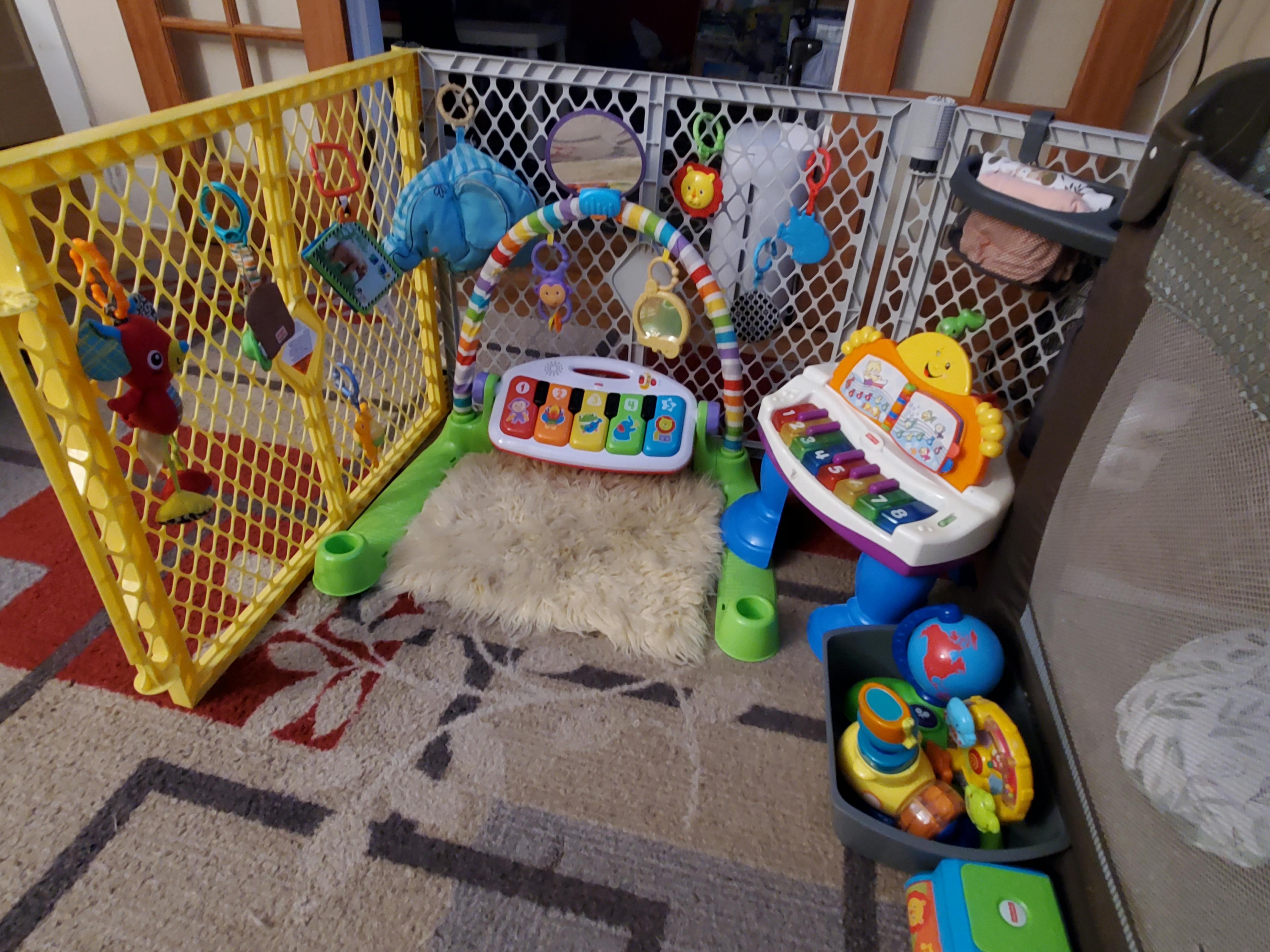 Baby play area with a yellow playpen, activity mat, and musical toys