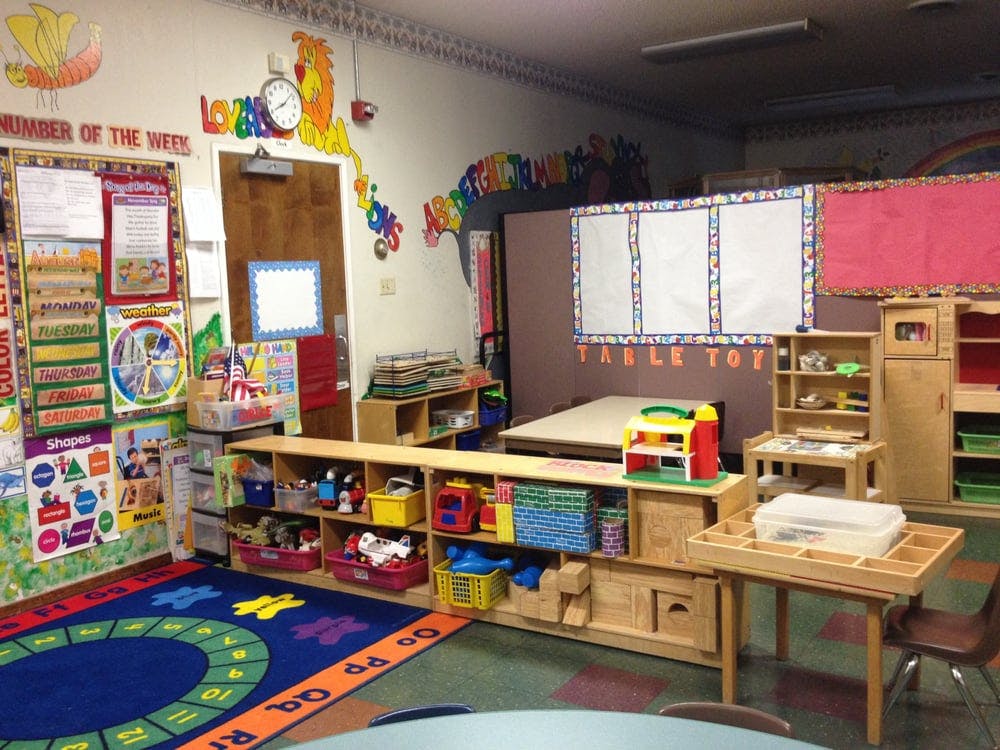 Classroom with colorful rug, shelves of toys, and educational posters