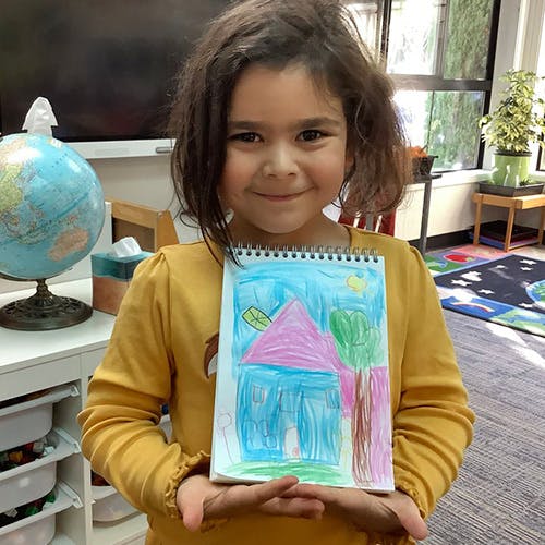 Child holding up a drawing of a house