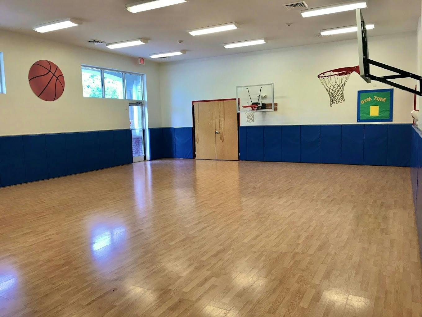 Basketball court in a gym with two hoops and "GYM TIME" sign