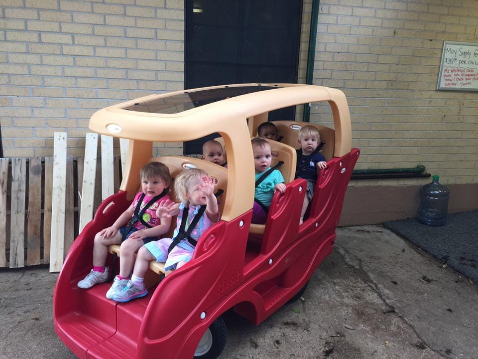 Multiple children sitting in a red and tan multi-seat stroller