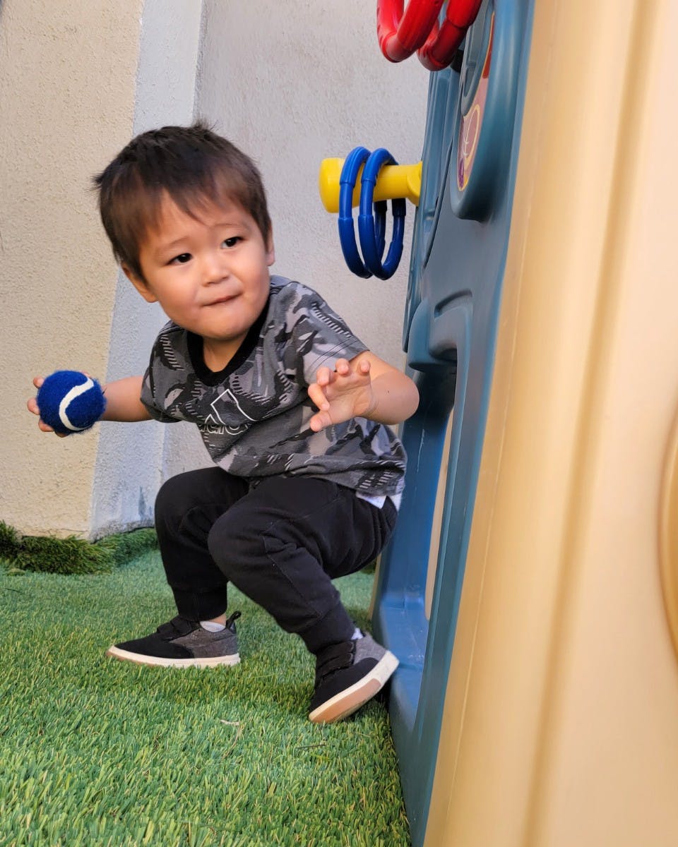 Child holding a blue ball while crouching on artificial grass