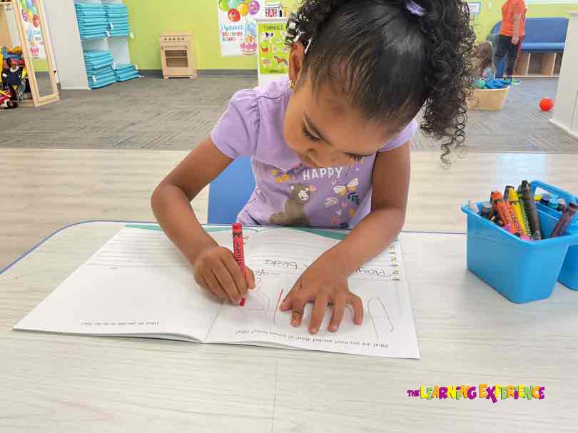 Child drawing in a book with a red crayon