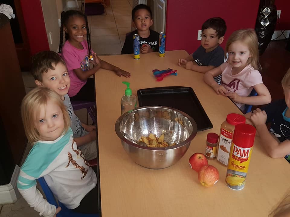 Multiple children sitting around a table with a bowl of food and apples