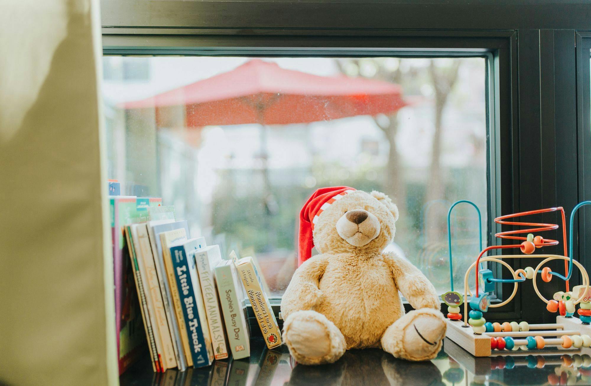 Teddy bear wearing a red hat next to books and a toy