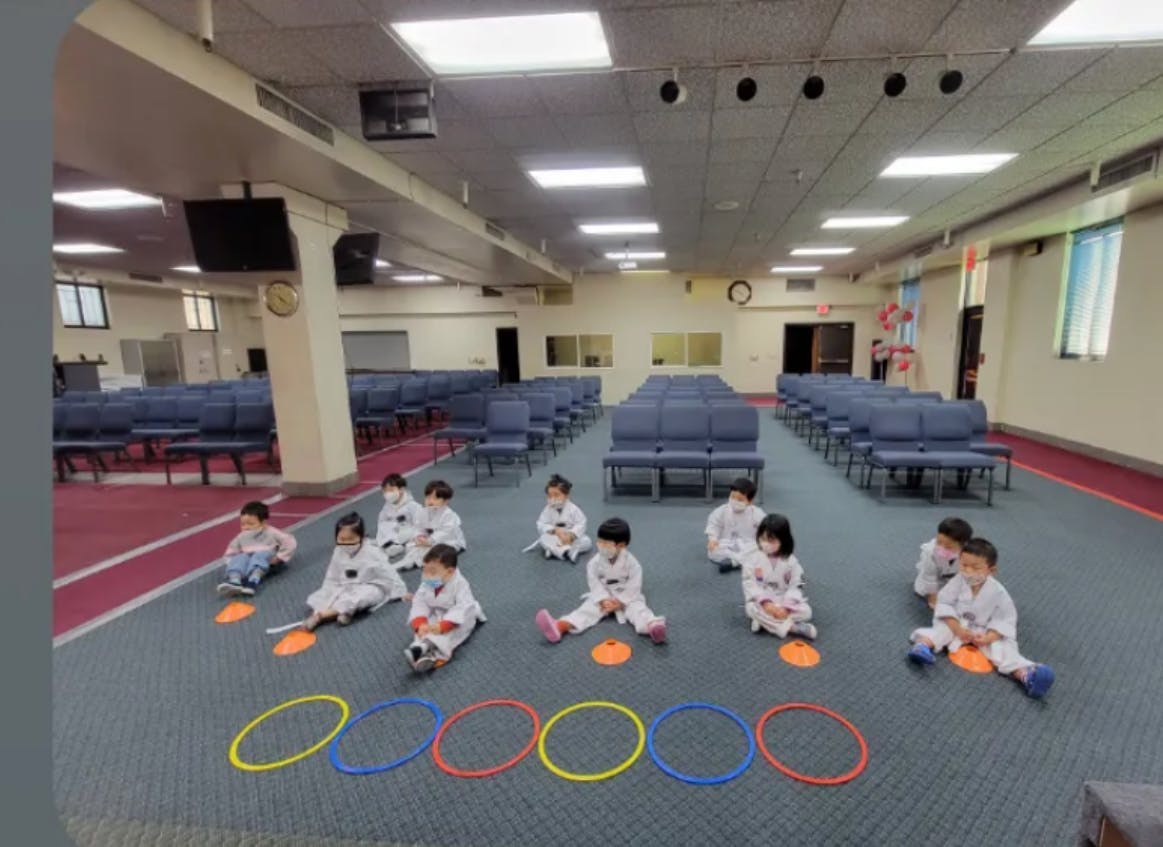 Children in white martial arts uniforms sitting on the floor with colorful rings