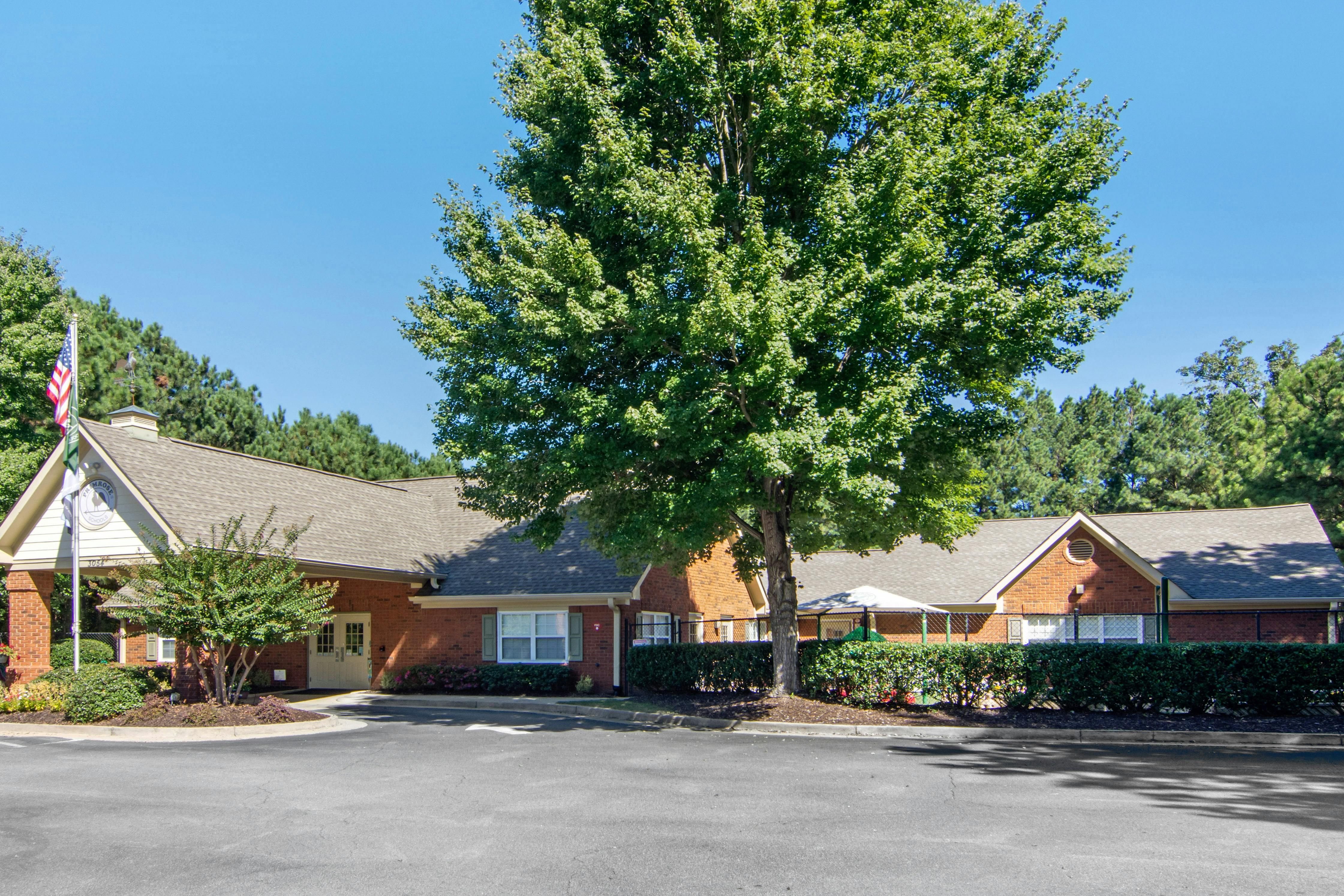 Brick building with a gray roof and a large green tree in front