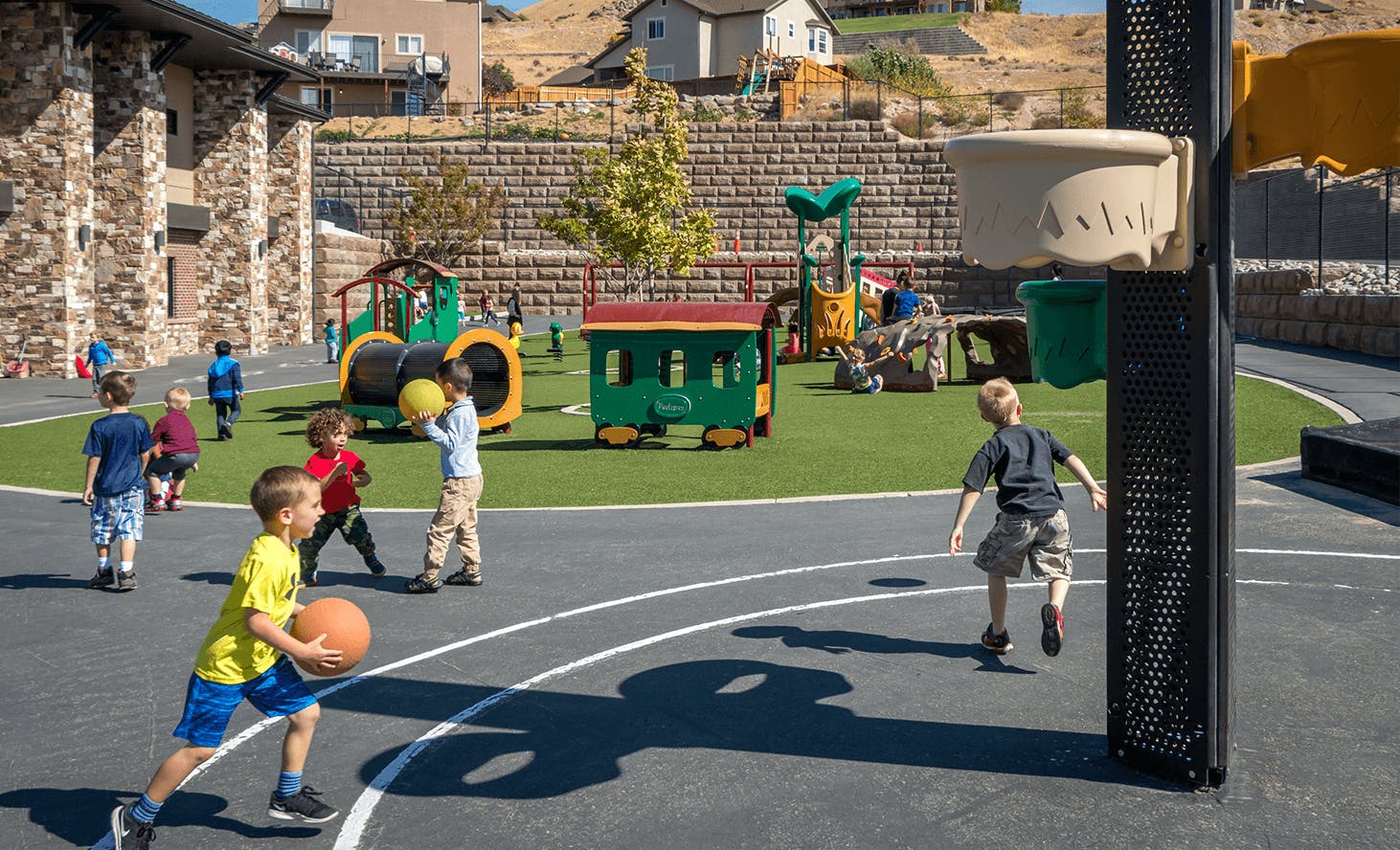 Children playing basketball on a court next to a playground