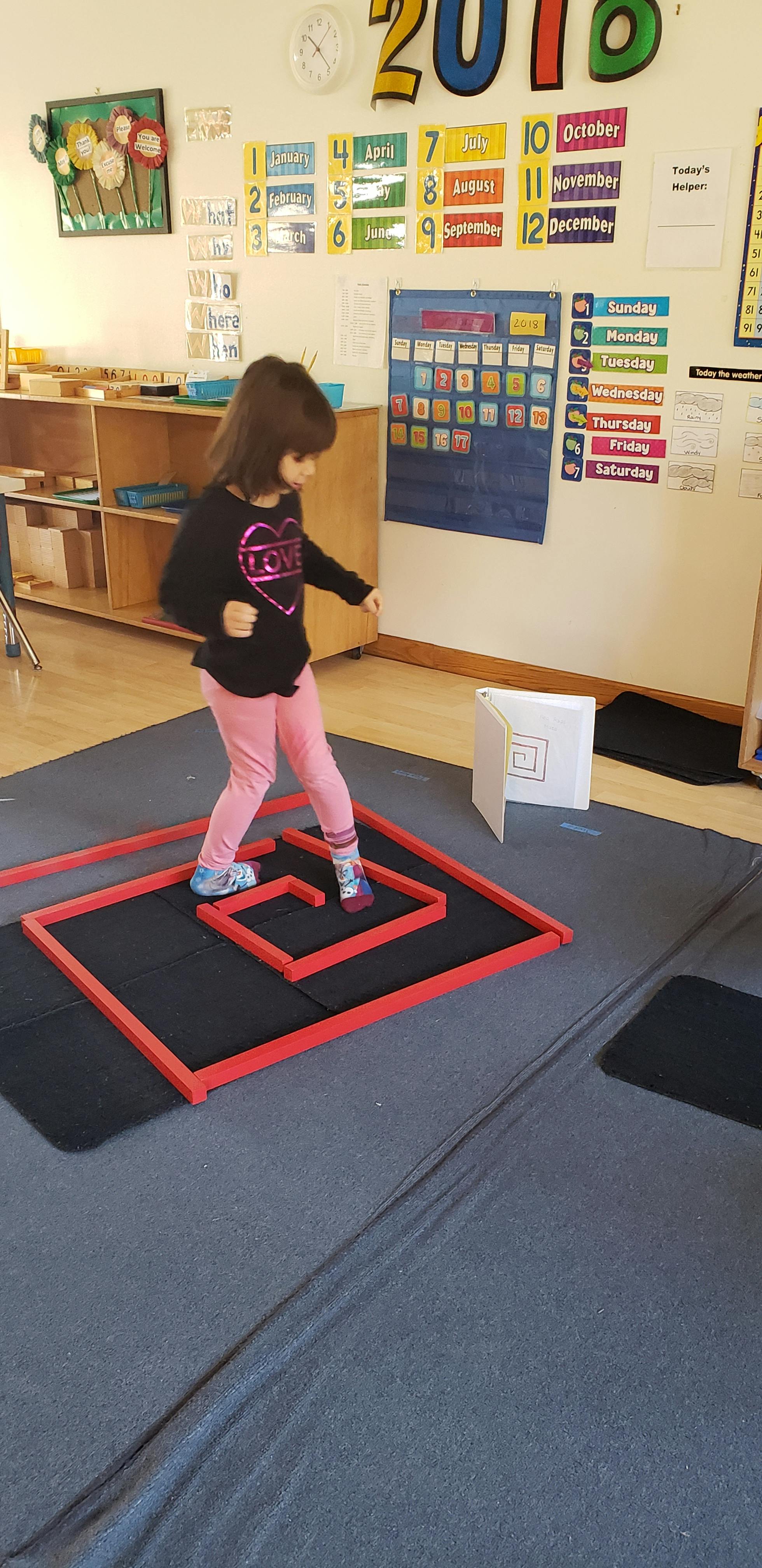 Child walking on a red square maze on the floor in a classroom