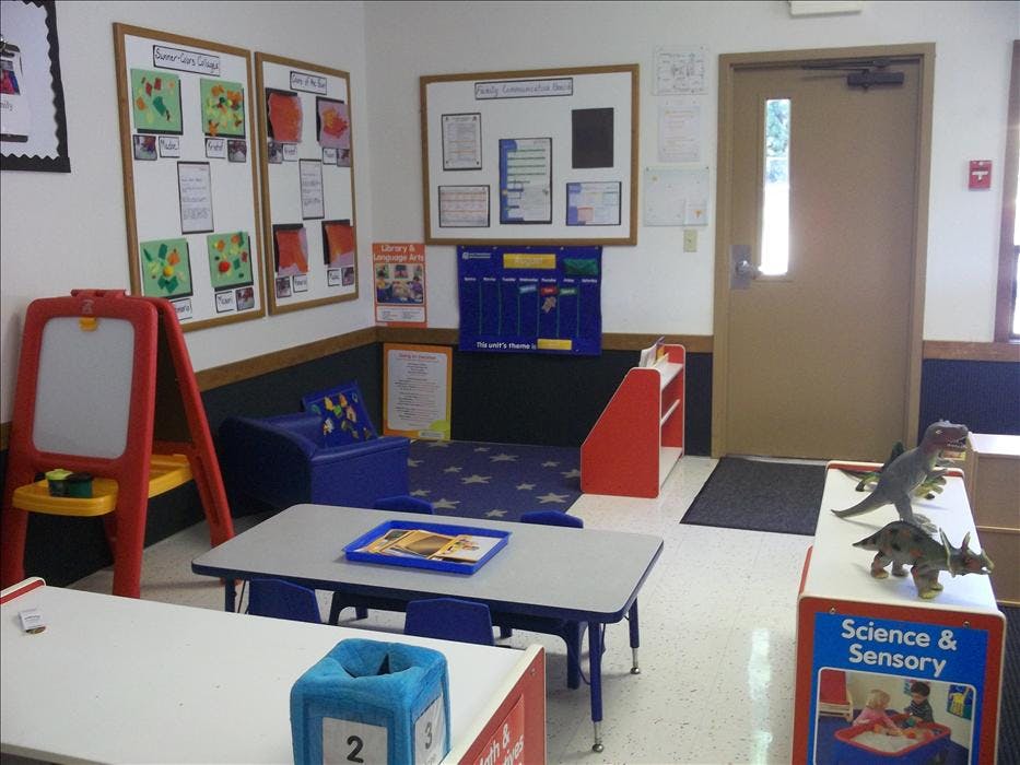 Classroom with children's artwork on walls, tables, and a reading nook