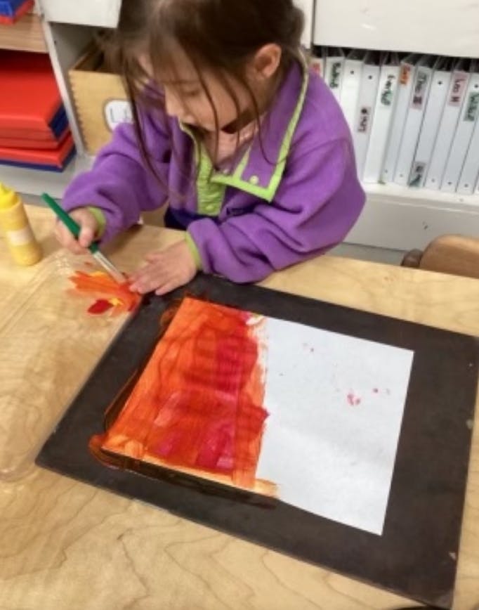 Child painting with a brush and red paint on paper