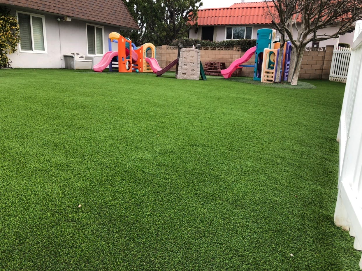Green artificial turf lawn with a playground in the background