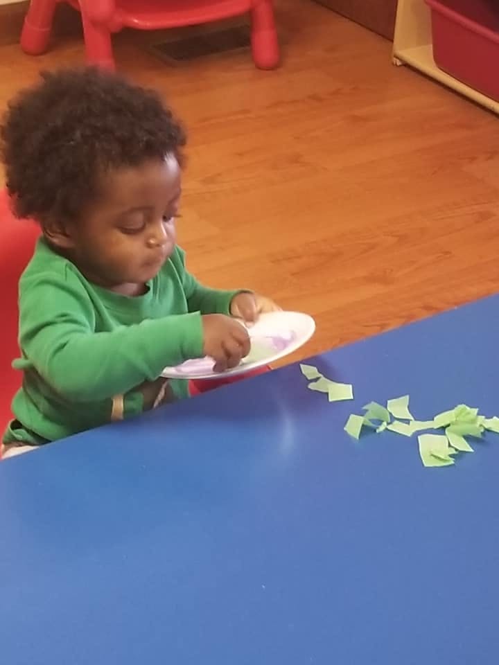 Child in a green shirt playing with a paper plate and green paper scraps