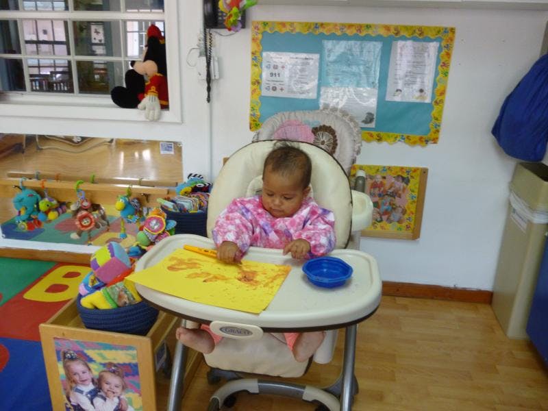 Child in a high chair drawing on yellow paper