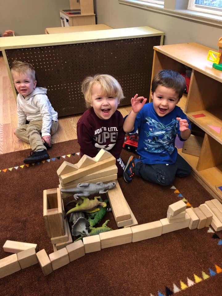 Three children playing with blocks and toy dinosaurs on a rug