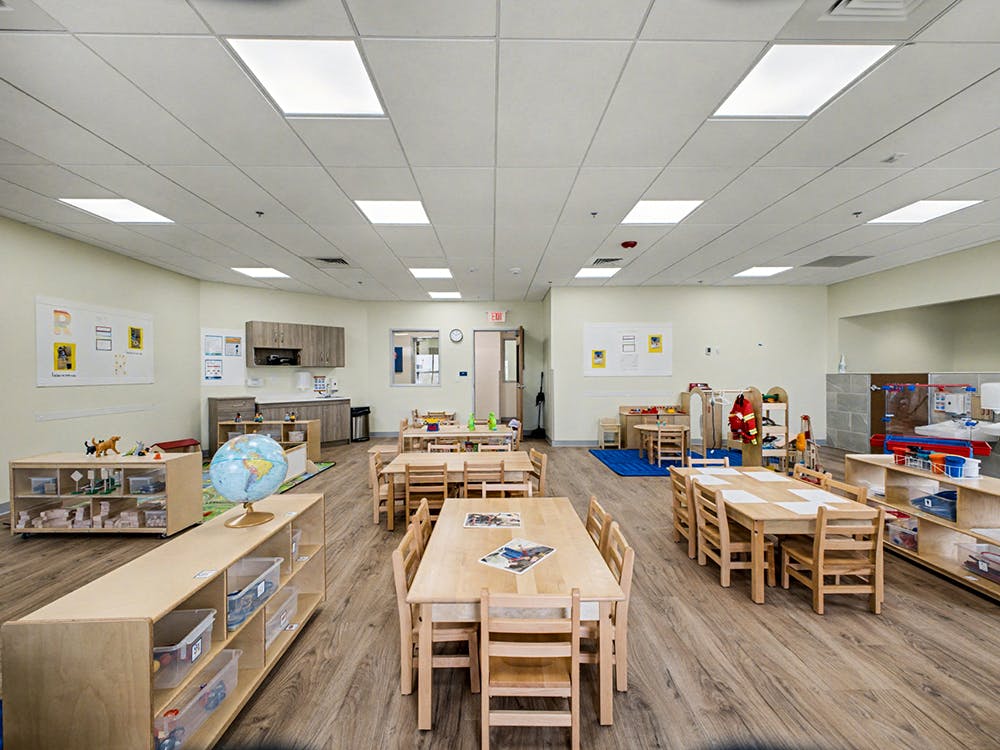 Empty classroom with small wooden tables and chairs, shelves with toys, and a globe