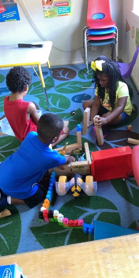 Three children playing with blocks on a patterned rug in a classroom