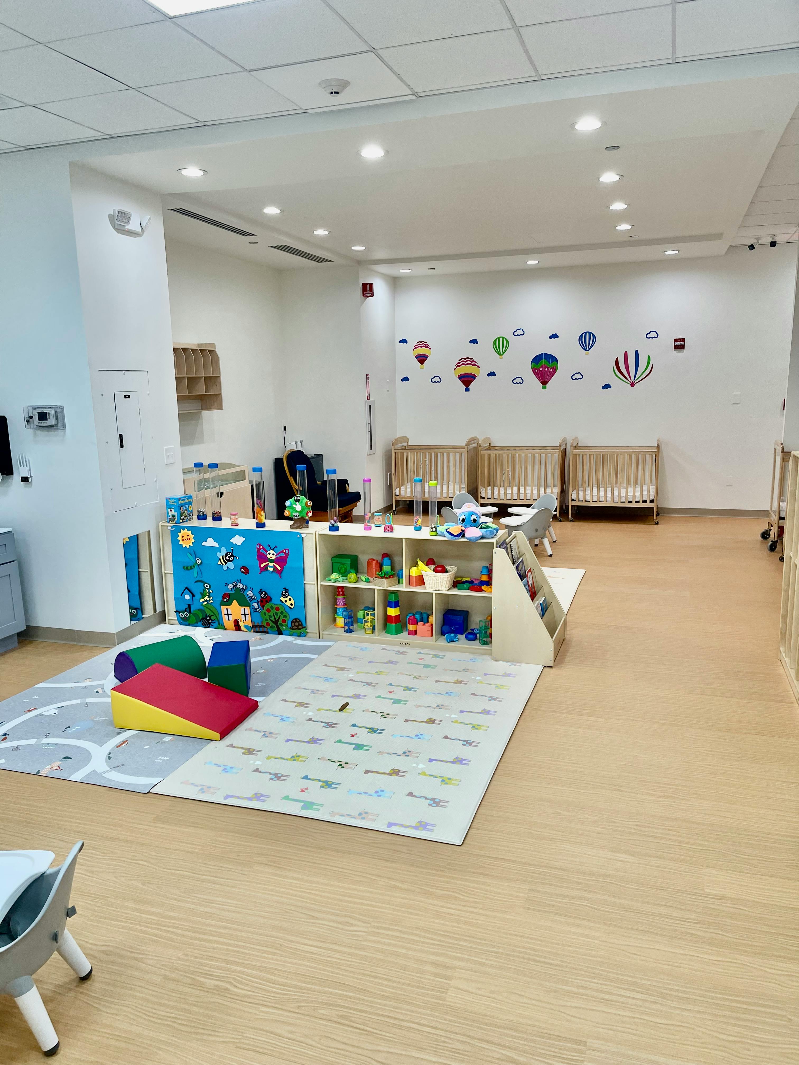 Daycare room with cribs, play mats, and shelves of toys
