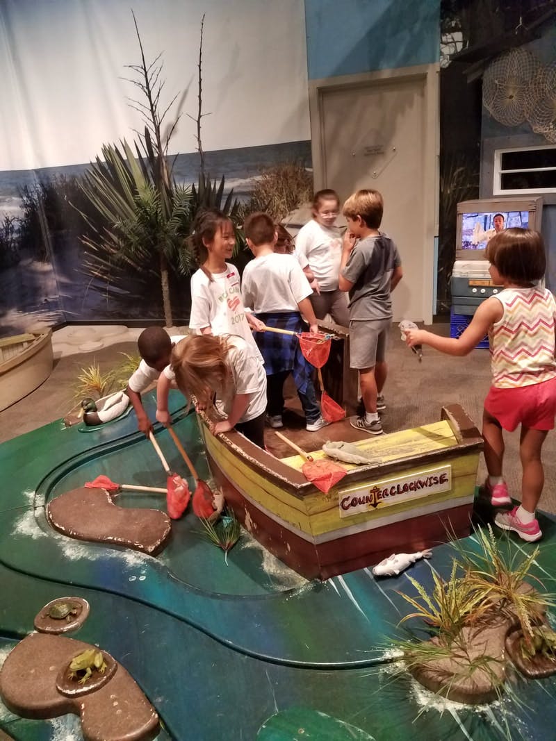 Children playing with a boat and fishing nets in an indoor exhibit