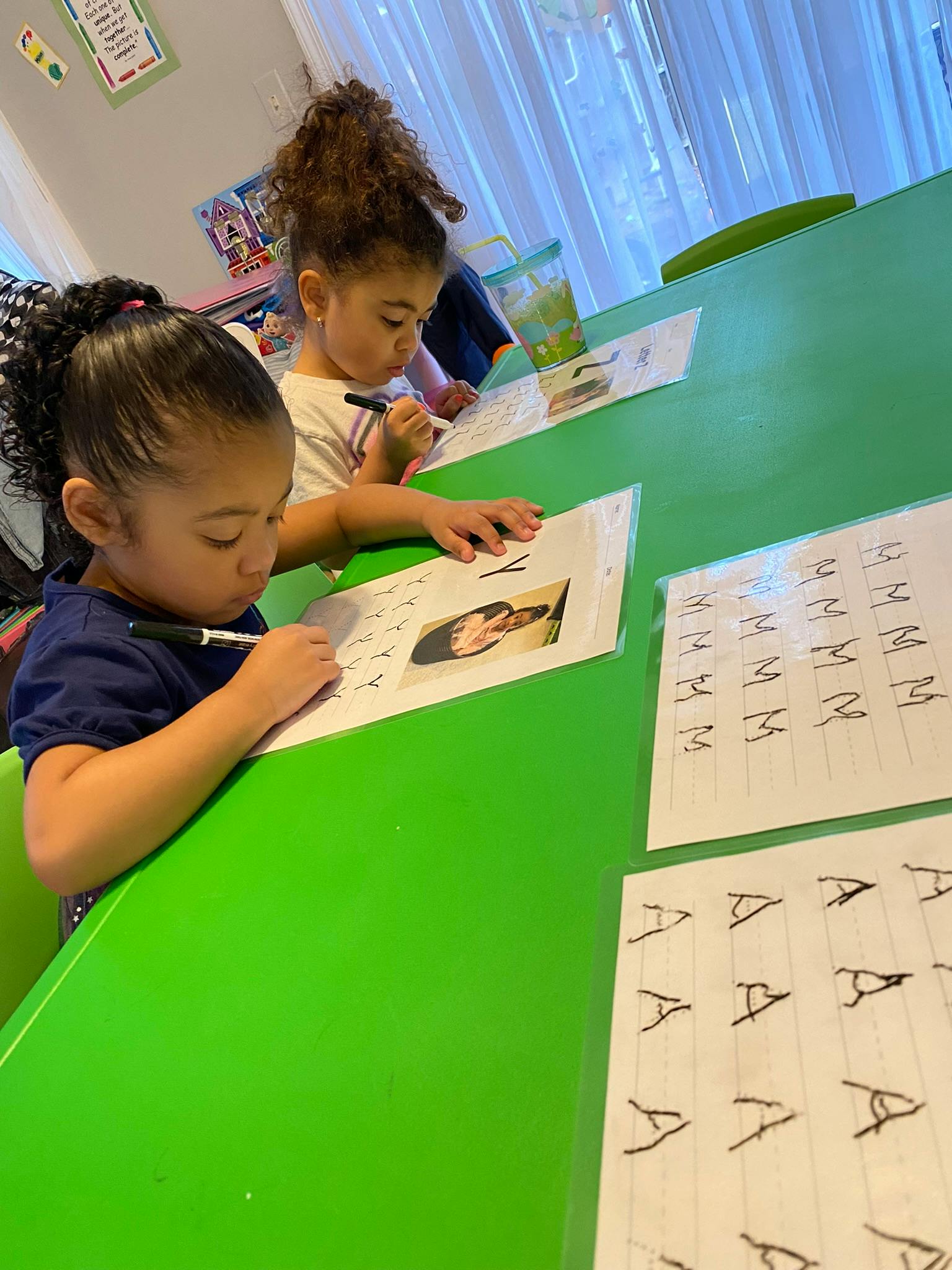 Two children writing on paper at a green table