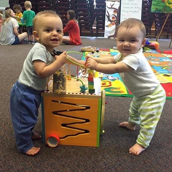 Two children playing with a wooden activity cube