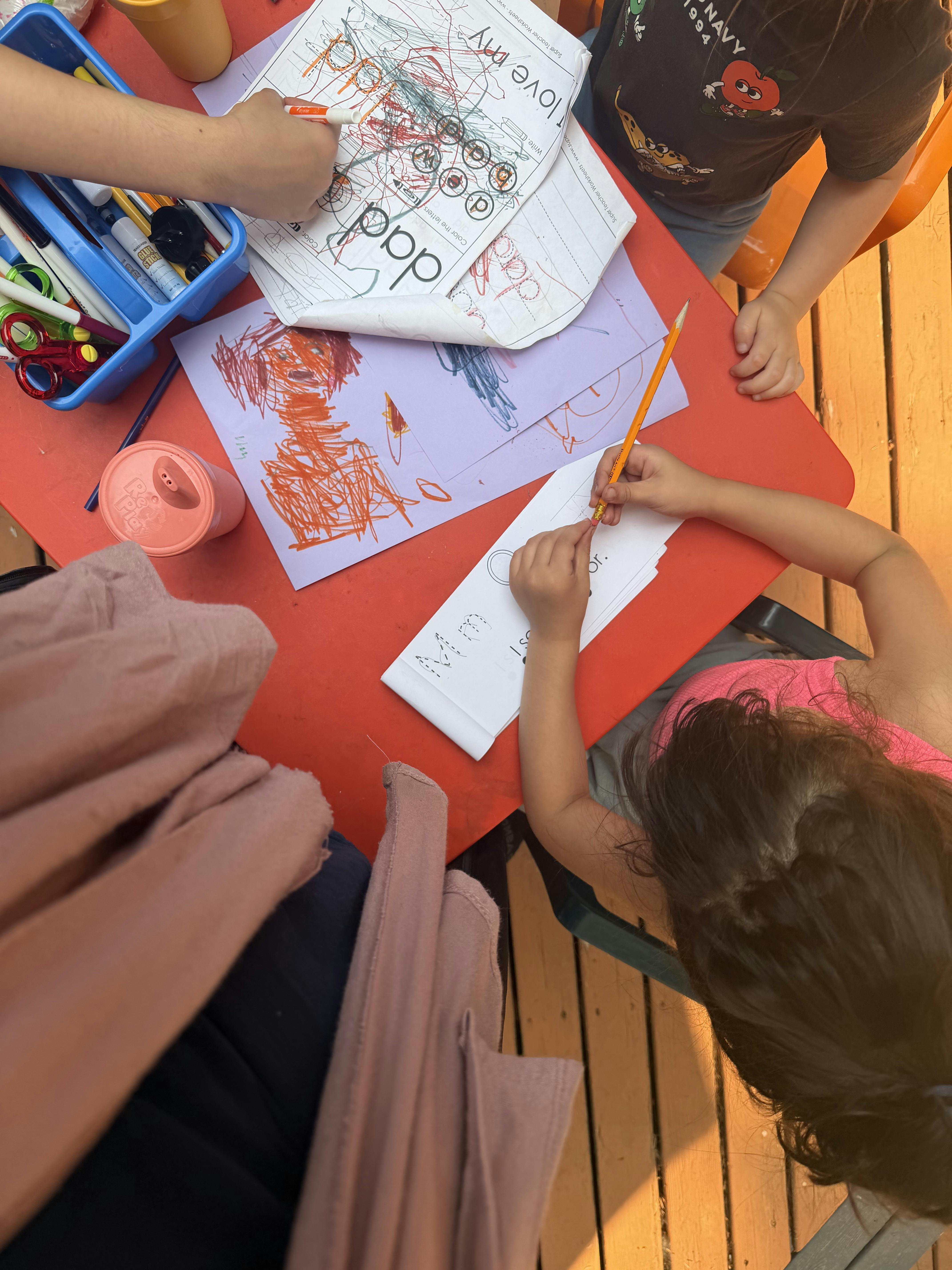 People using pencils and markers to complete worksheets at a red table