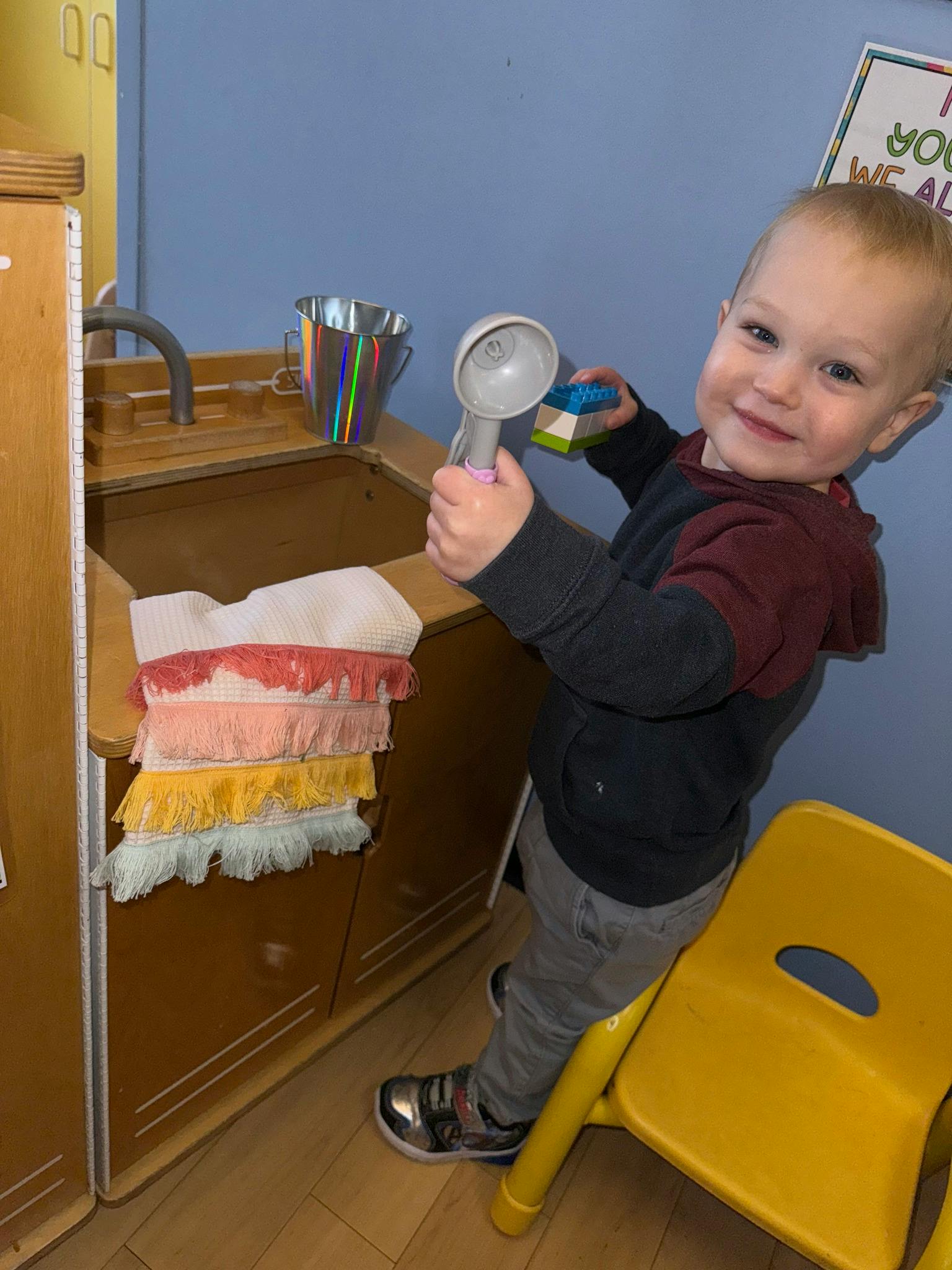 Child holding a toy ice cream scoop and sponge in a play kitchen