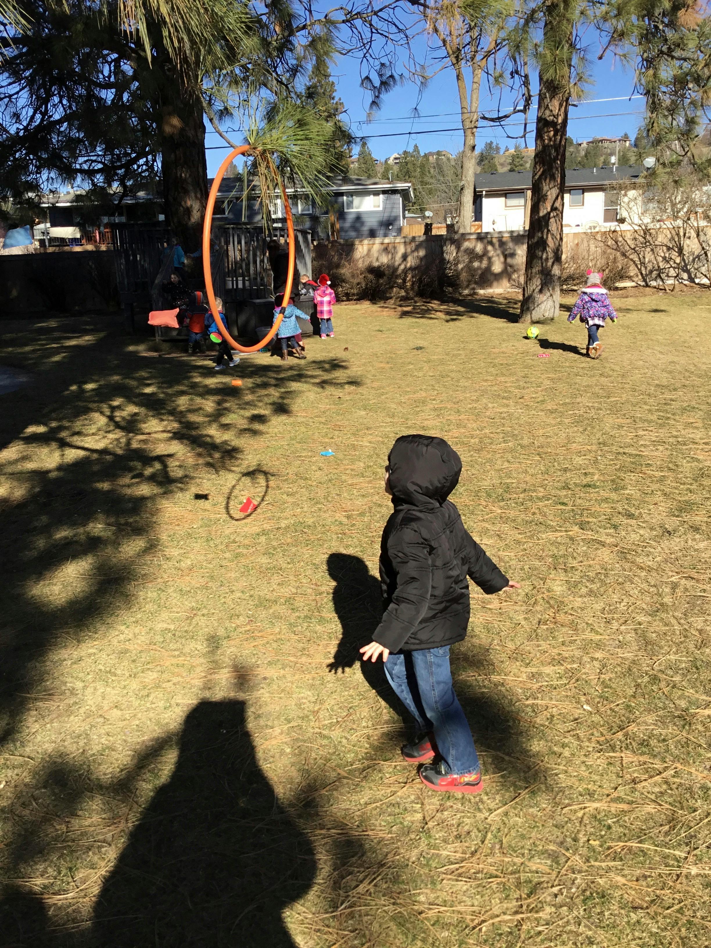 Child in a black jacket and jeans walking in a grassy backyard