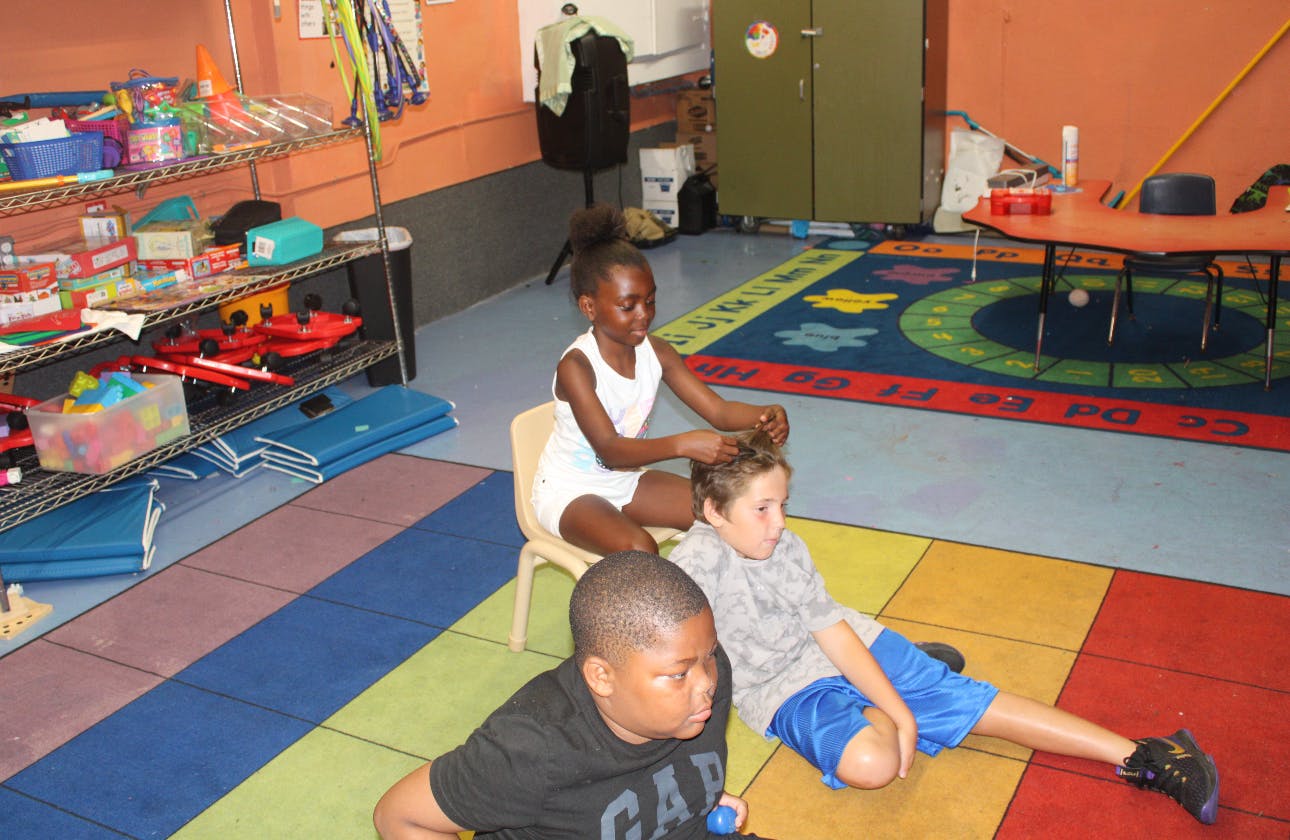 Child sitting on chair styling hair of another child on the floor