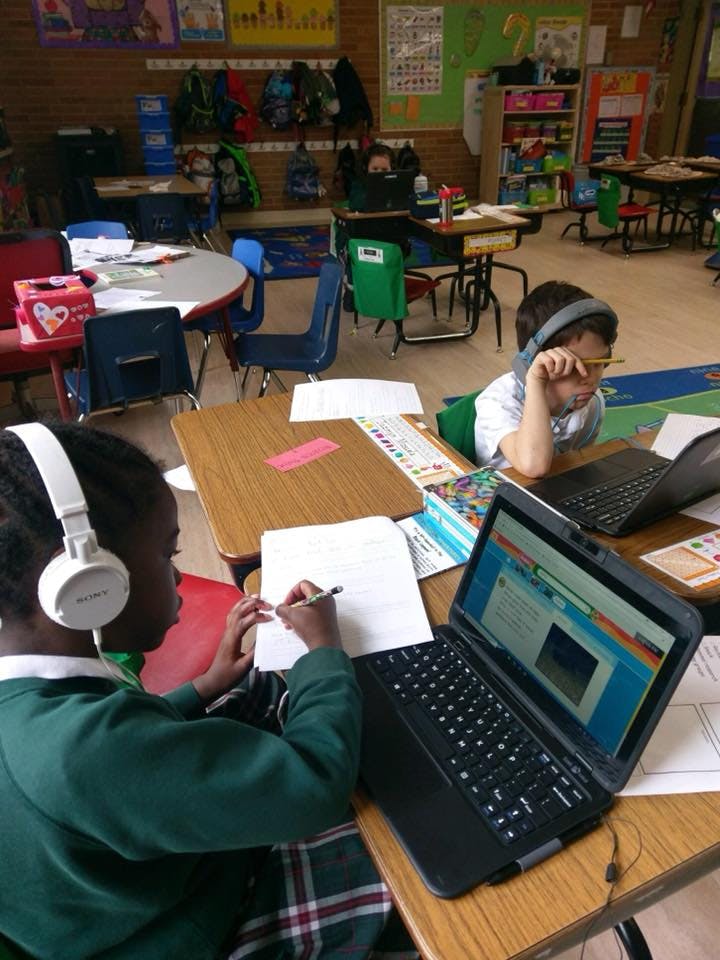 Two children with headphones using laptops in a classroom