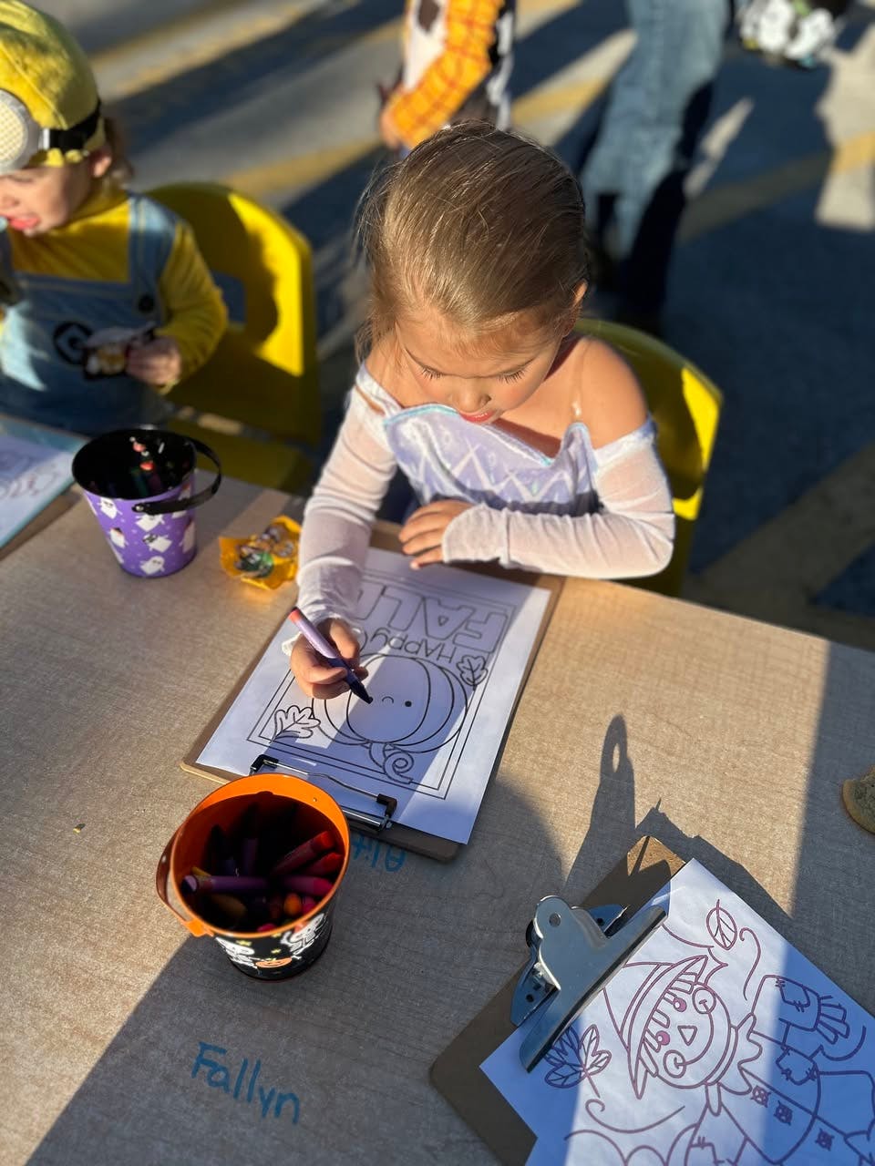 Child in a costume coloring a sheet on a clipboard at a table