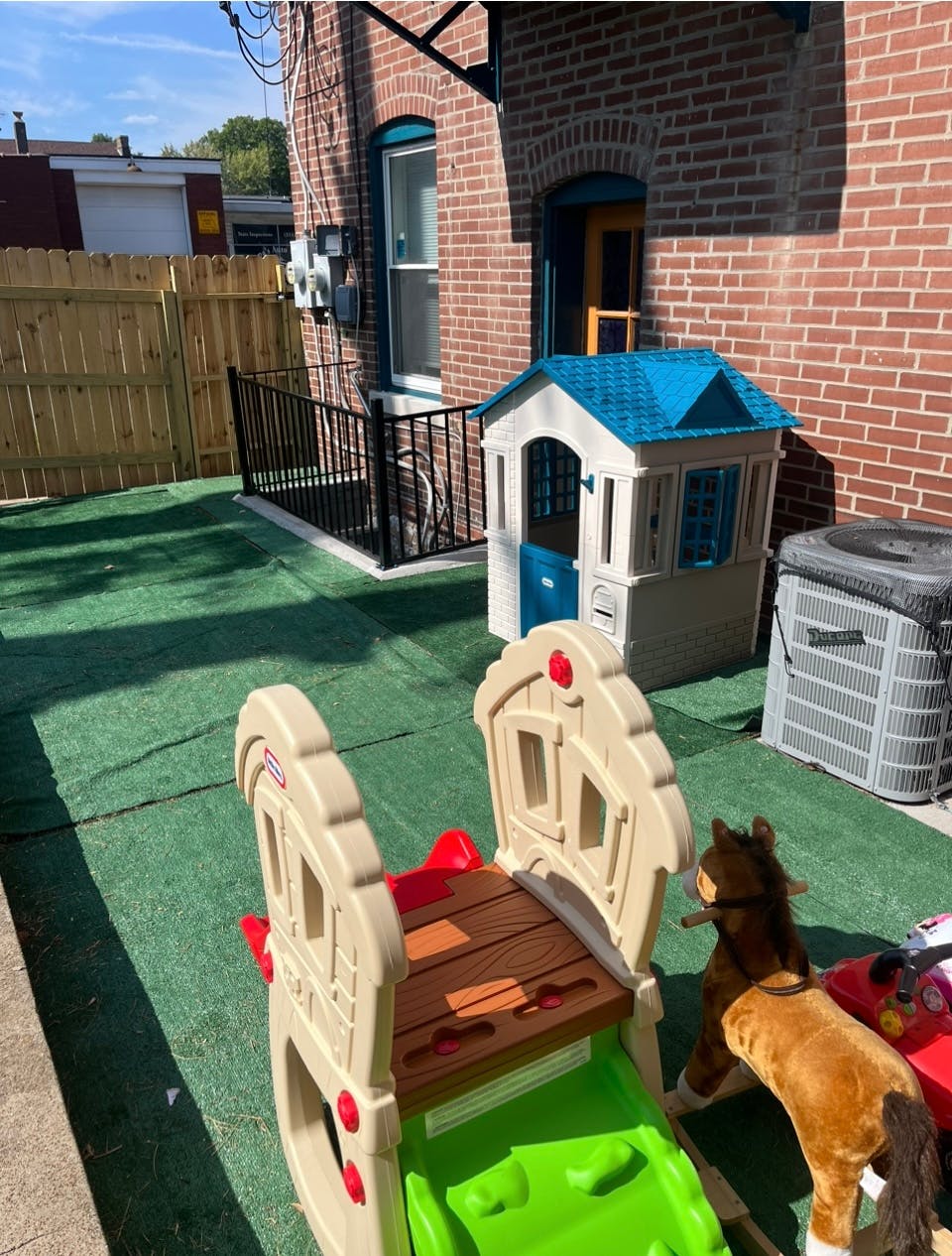 Playhouse and slide on artificial turf next to a brick building