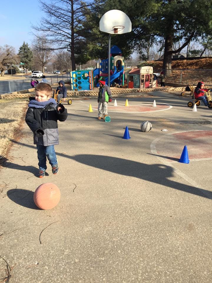 Child in winter coat standing on playground with a ball