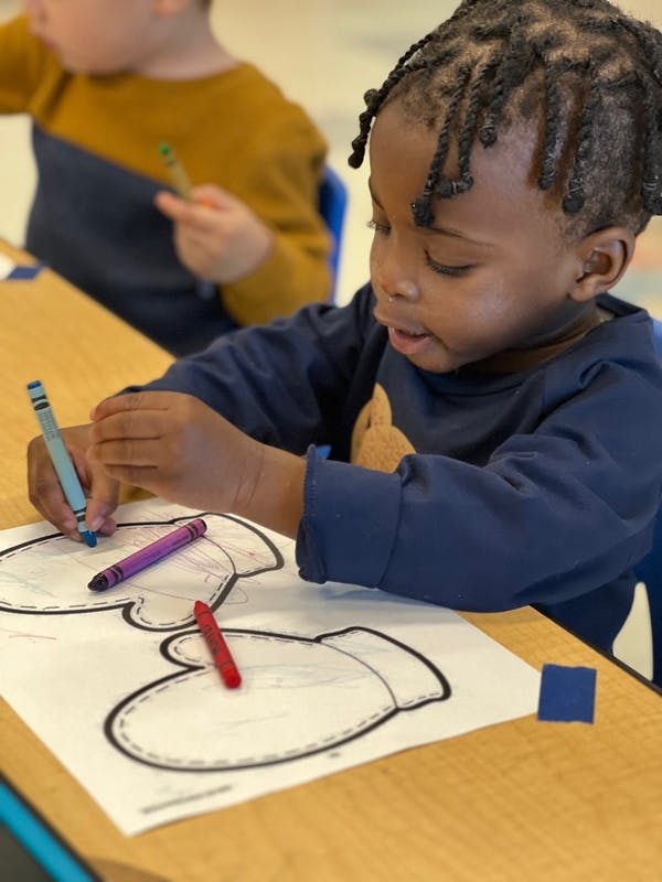 Child coloring a mitten outline with a crayon at a table