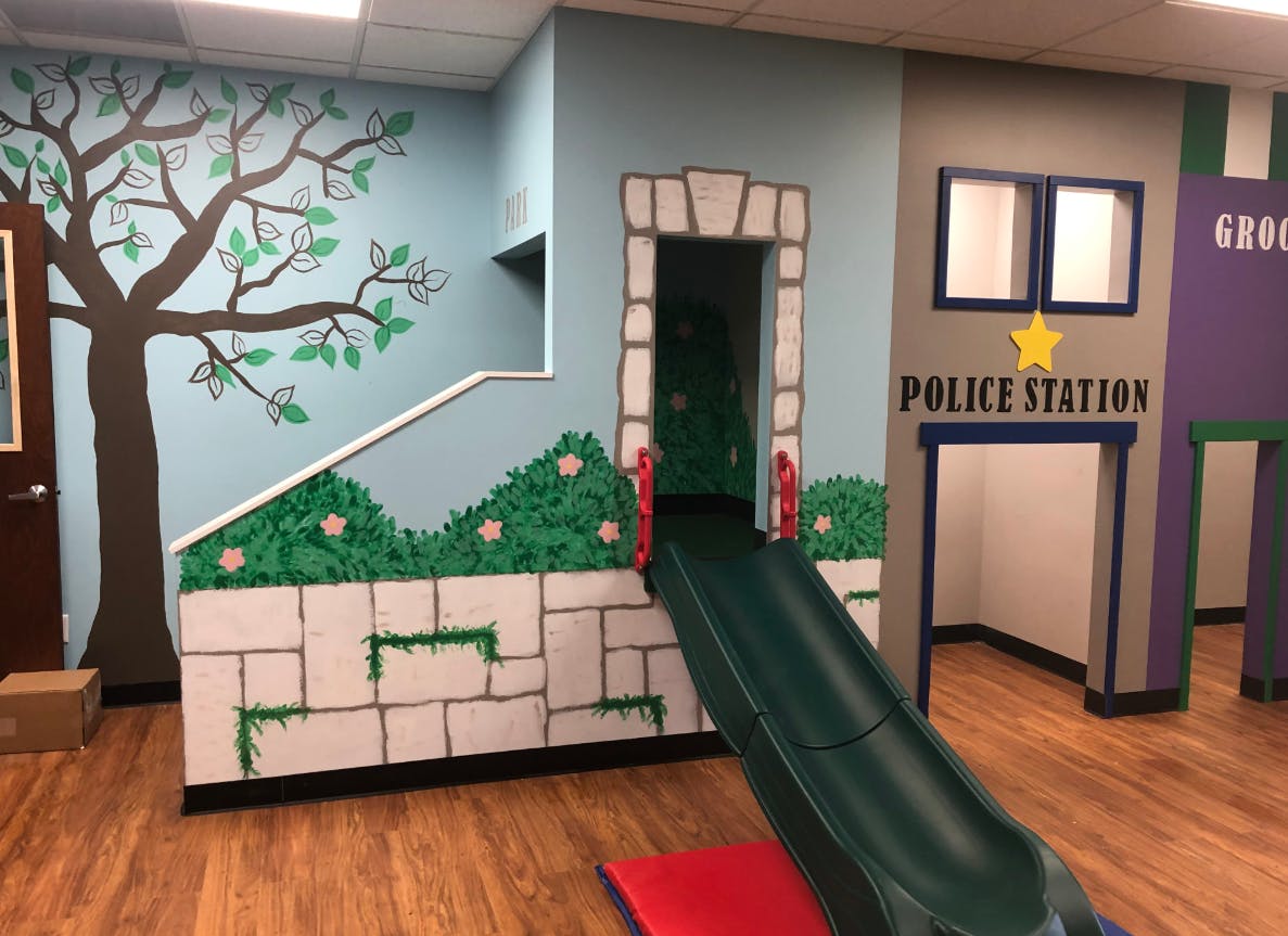 Indoor play area with a slide, tree mural, and a play police station