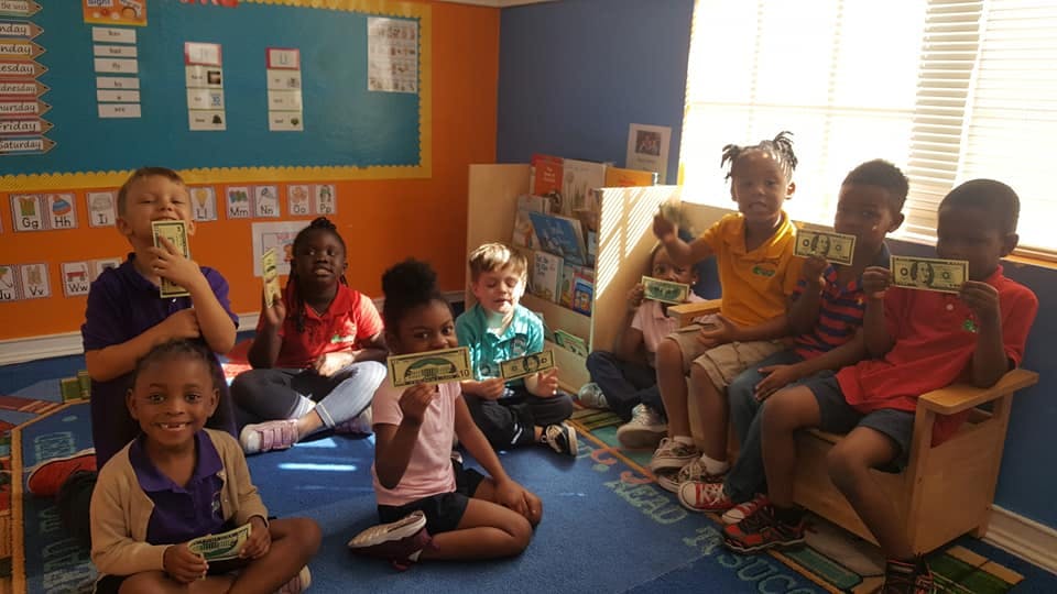 Children holding up play money in a classroom