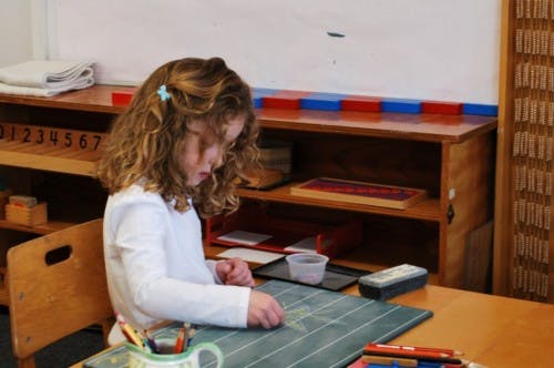 Child drawing on a chalkboard at a desk in a classroom