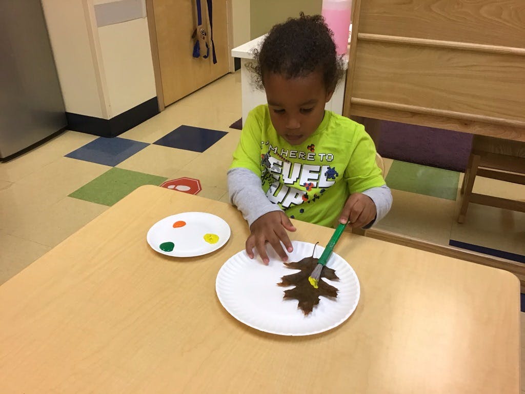 Child painting a leaf on a paper plate