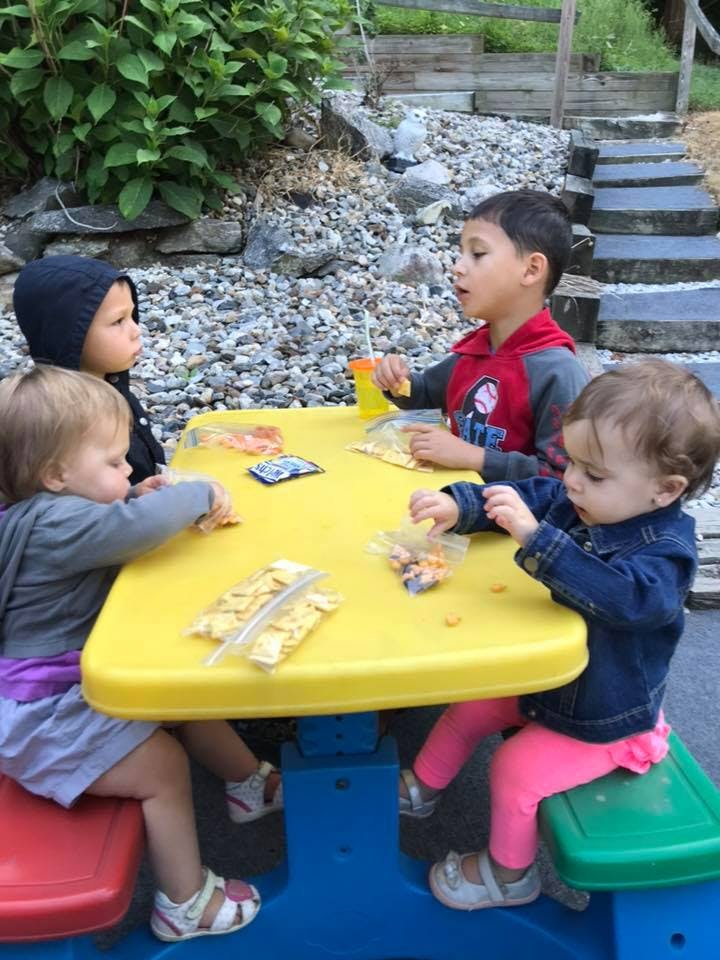 Four children sitting at a yellow table outdoors