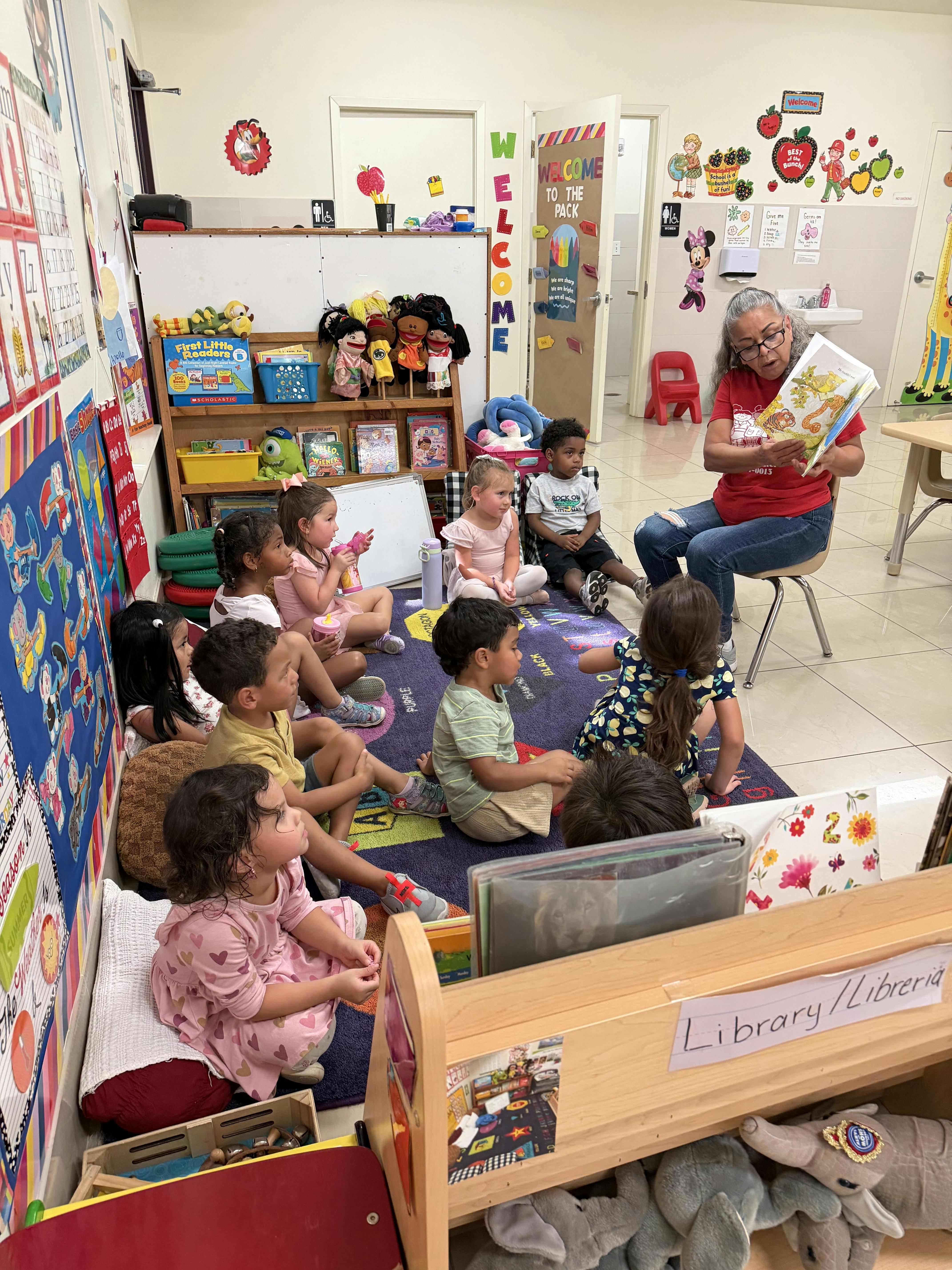 Adult reading a book to a group of children sitting on a classroom rug