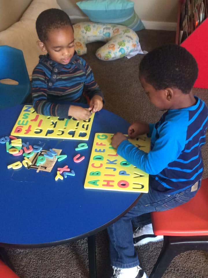 Two children playing with alphabet letter puzzles at a table