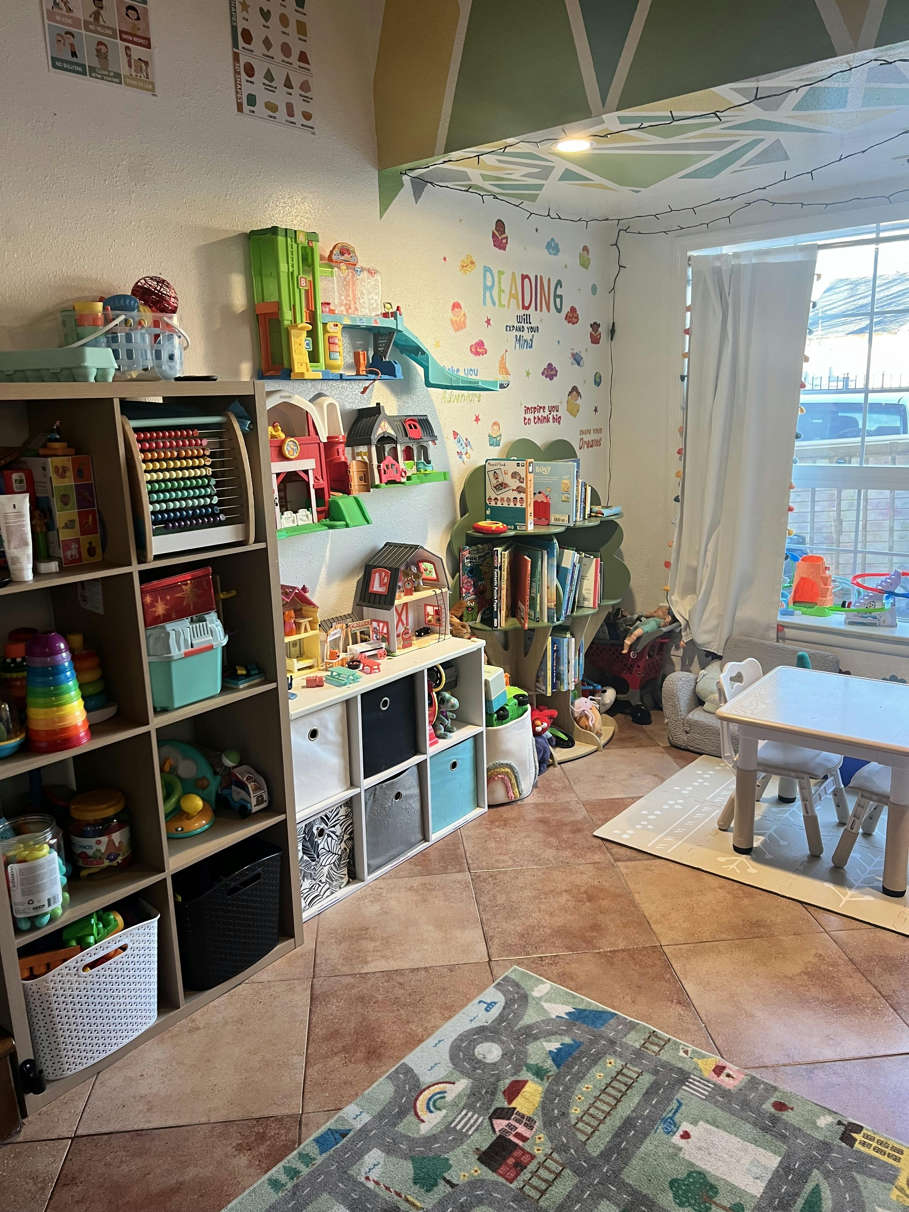 A children's playroom with shelves full of toys, books, and a small table and chairs