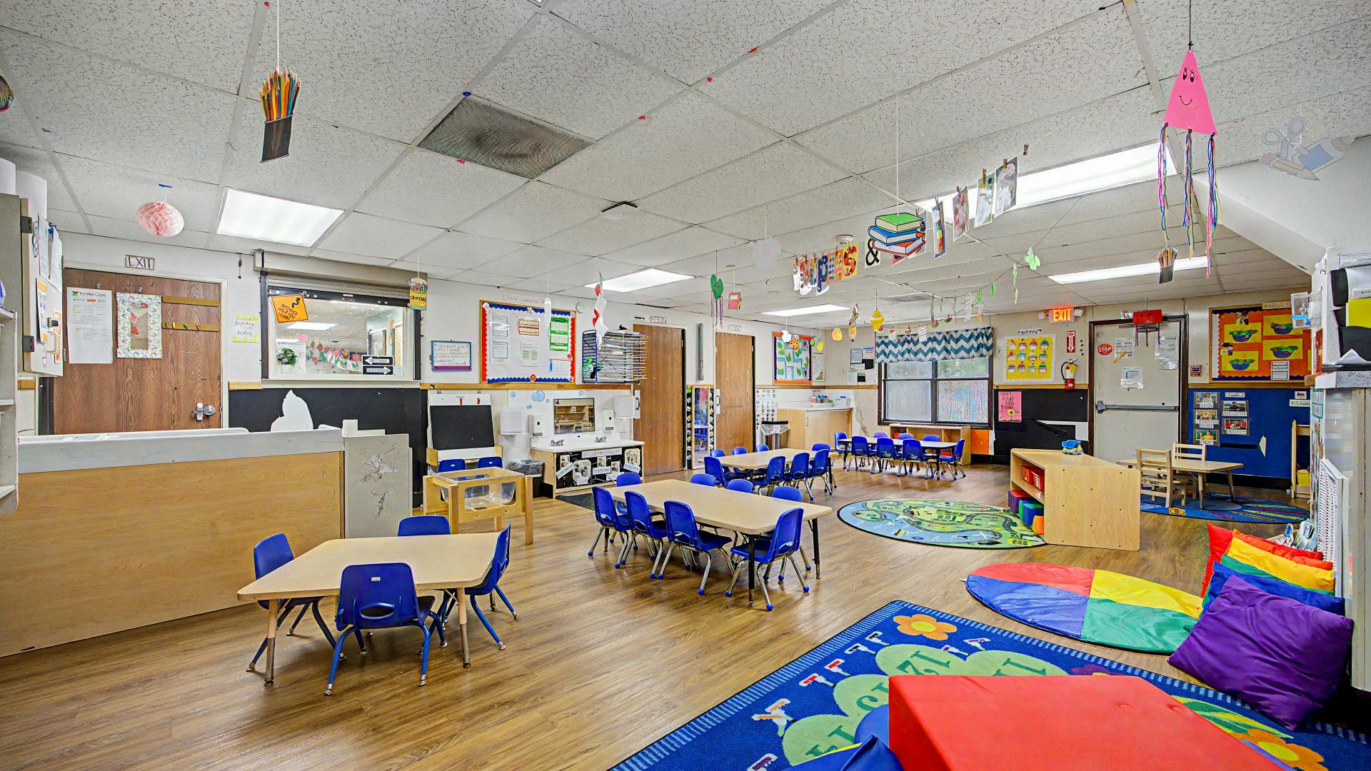 Empty classroom with small tables and chairs, colorful rugs, and decorations