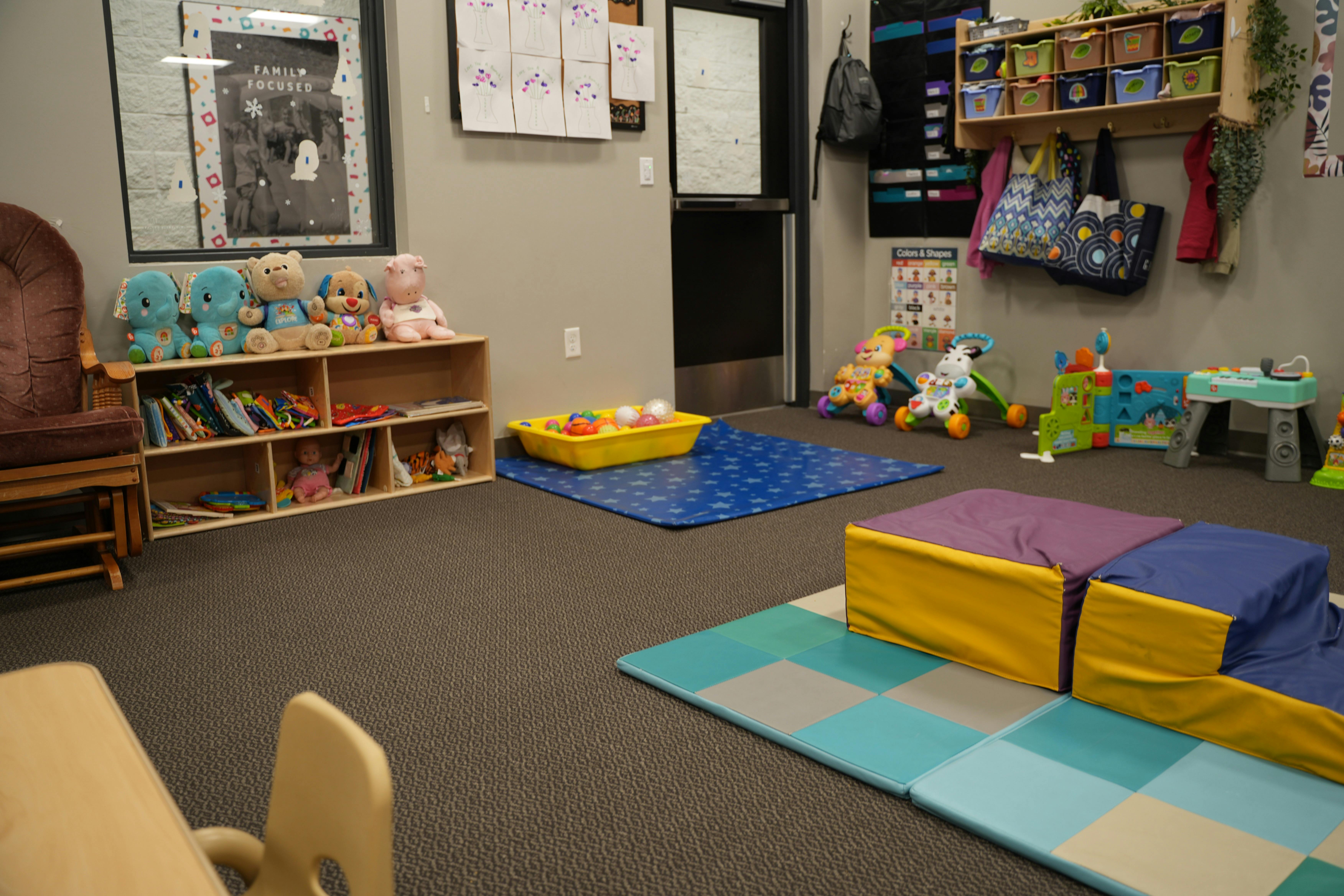 A playroom with child-sized toys, shelves, and soft play mats