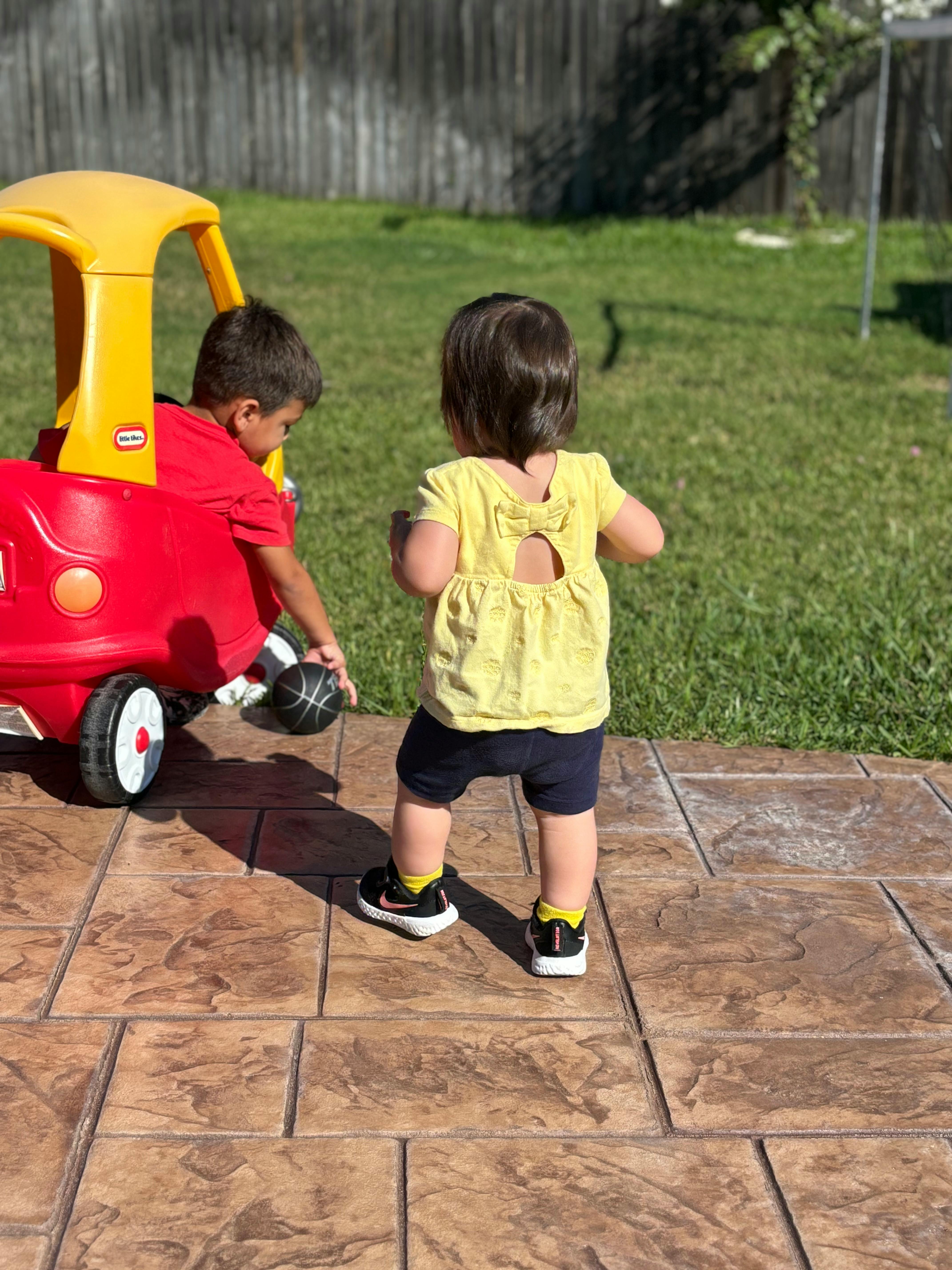 Two children playing with a toy car and a ball outdoors