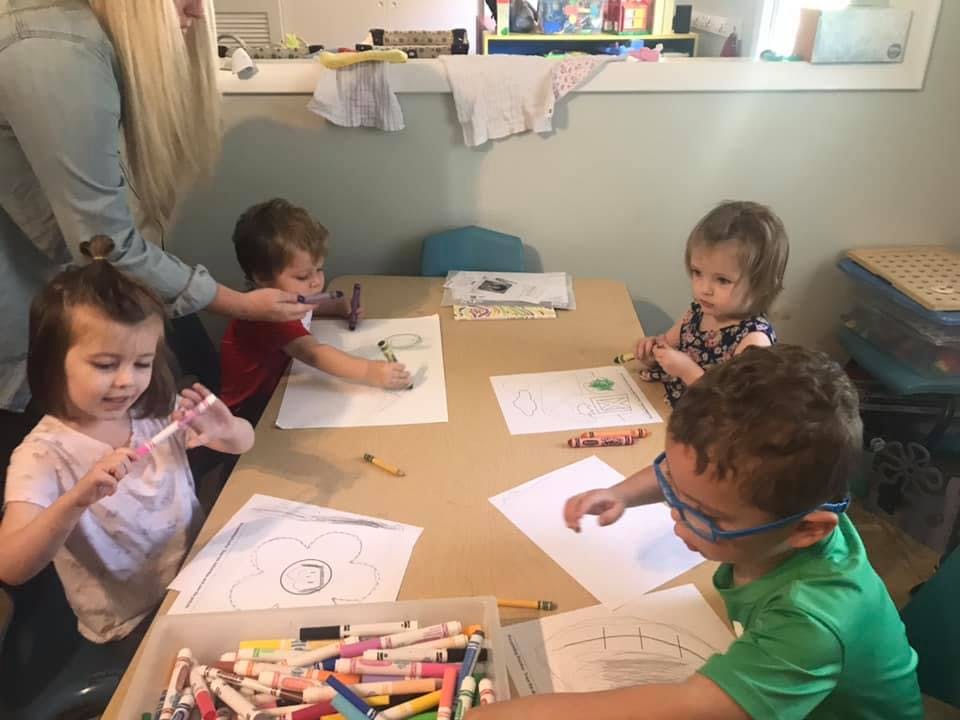 Adult helping children draw at a table