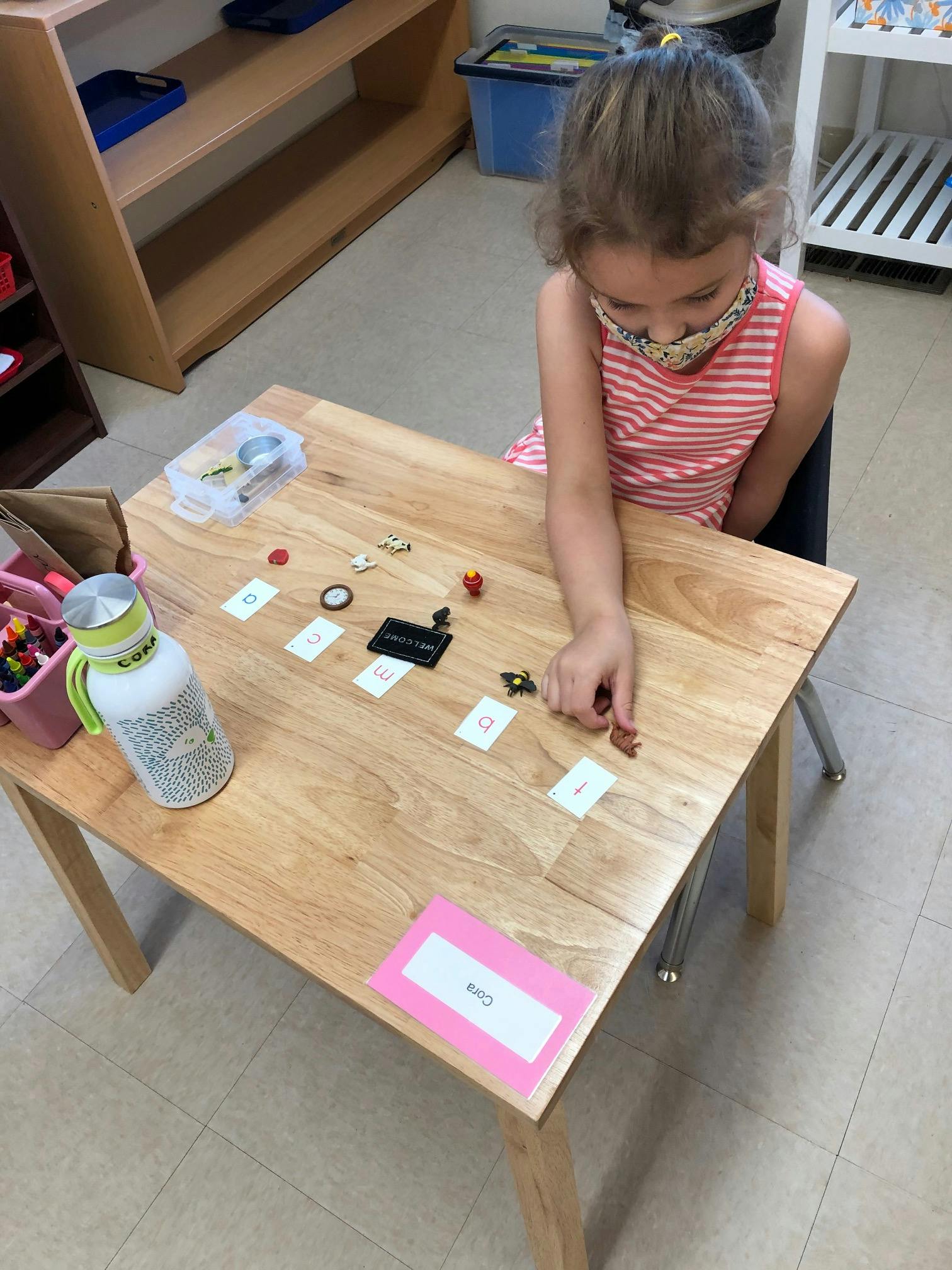 Child in a mask playing with small objects on a wooden table