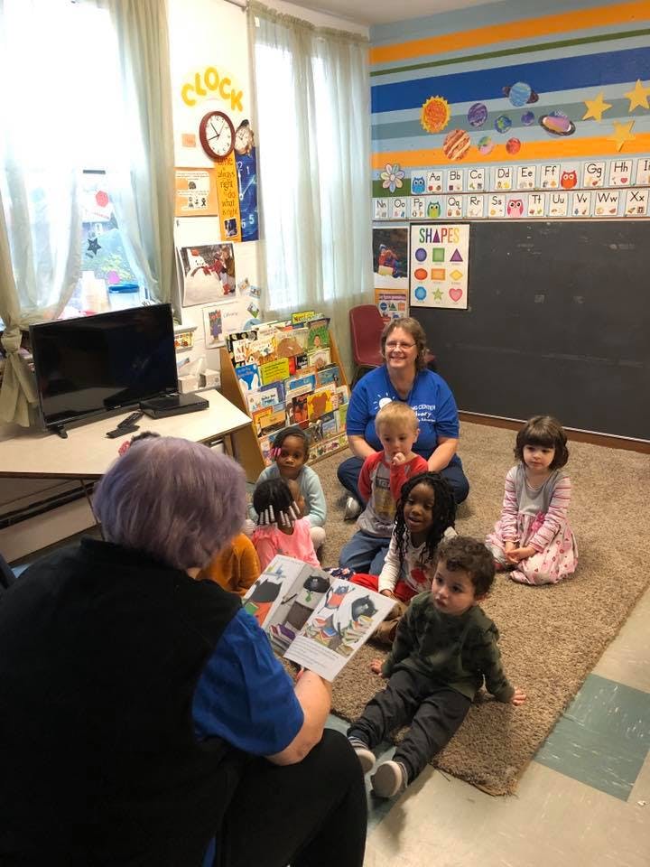 Adult reading a book to a group of children in a classroom
