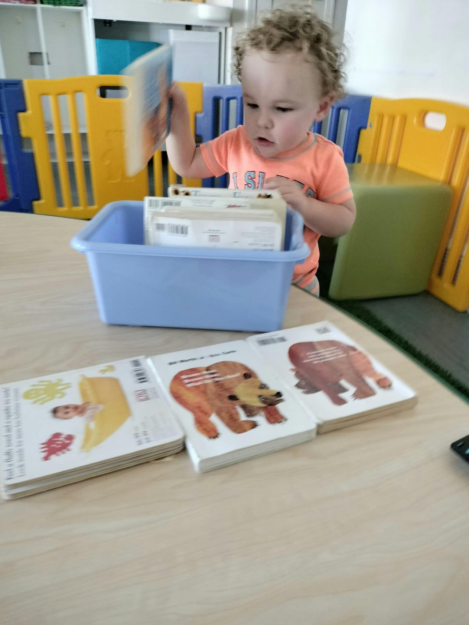 Child holding a book over a blue bin with other books
